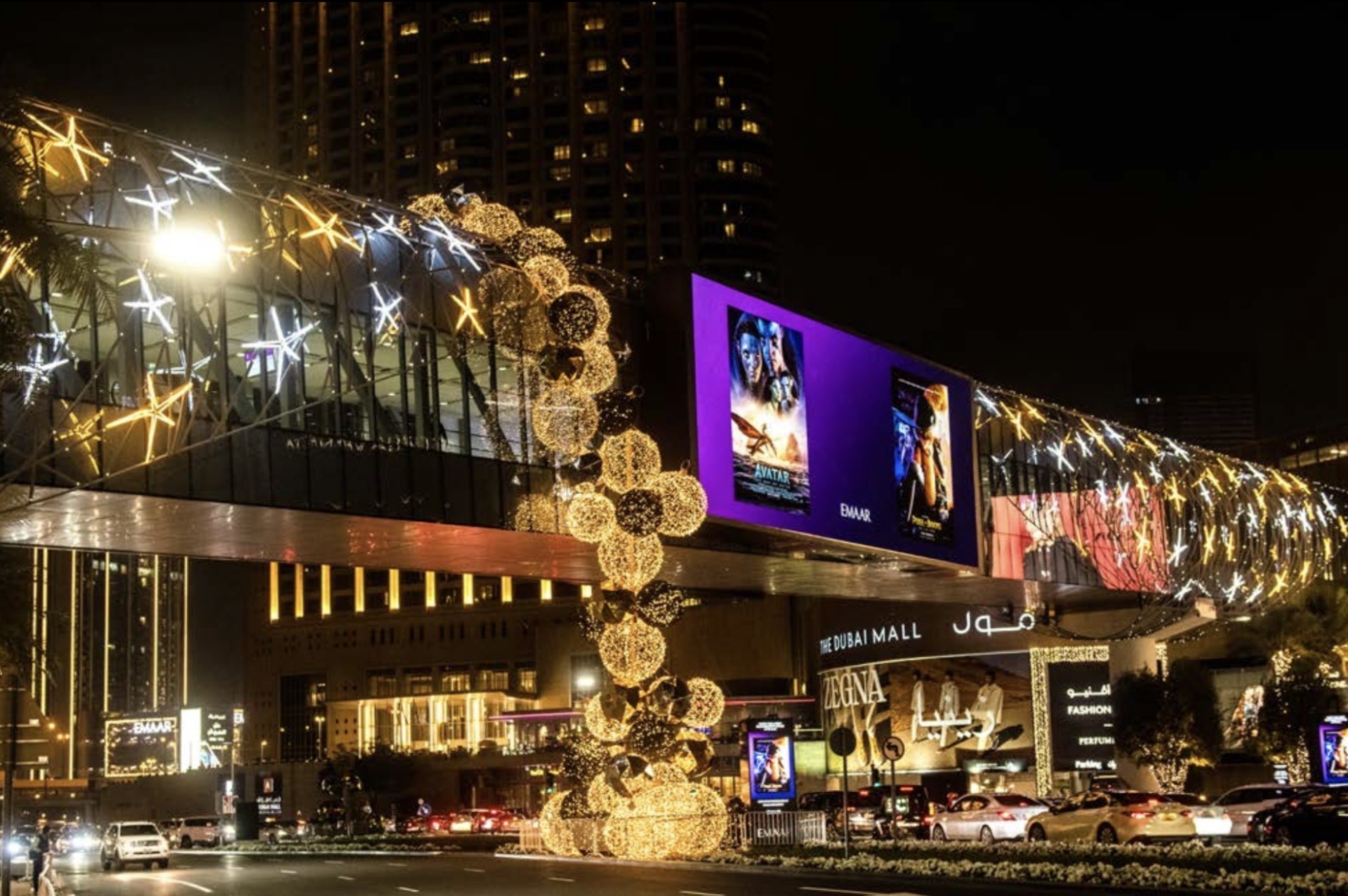 Illuminated skybridge and suspended golden spheres outside The Dubai Mall at night